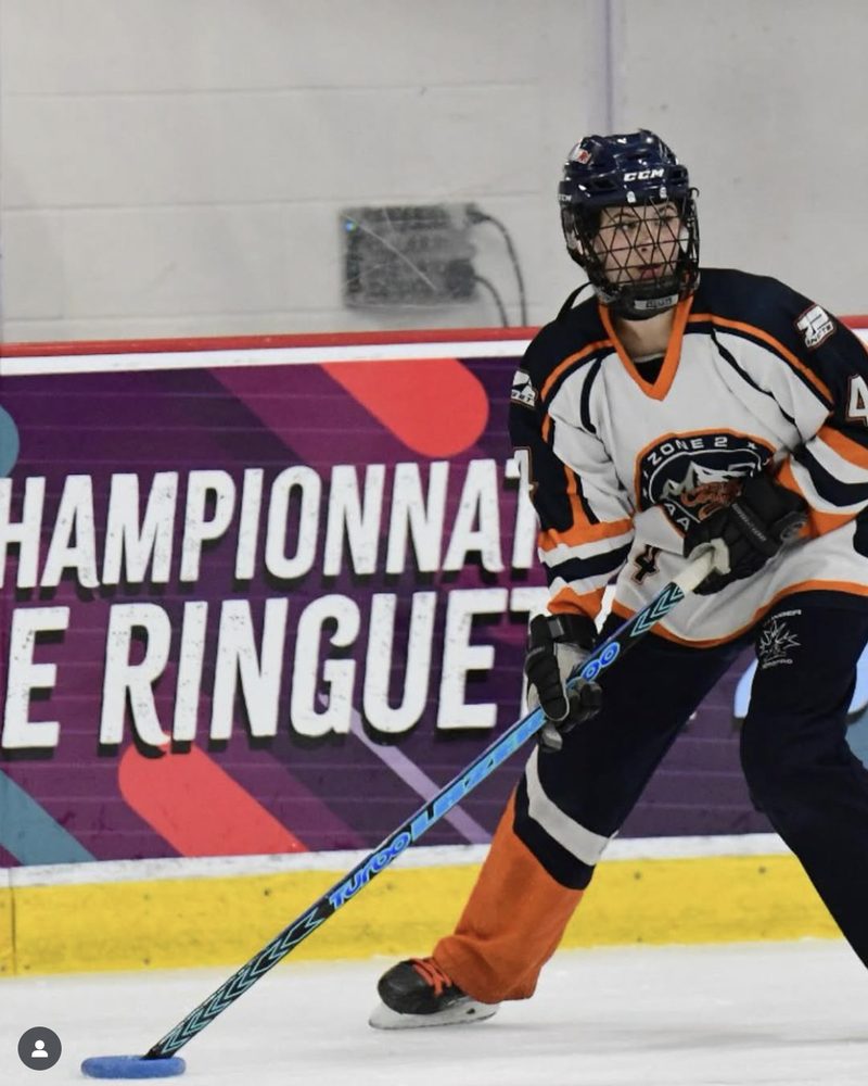 Ringette player driving forward at a Championnat de Ringuette banner